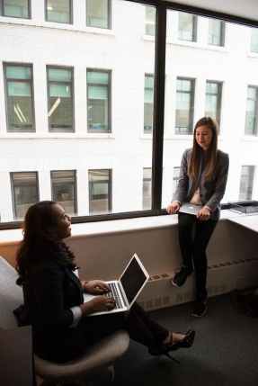 two women talking white holding laptop computers